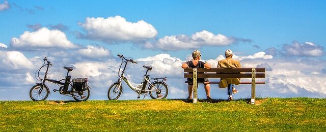 青空の下のベンチに座っている夫婦と自転車